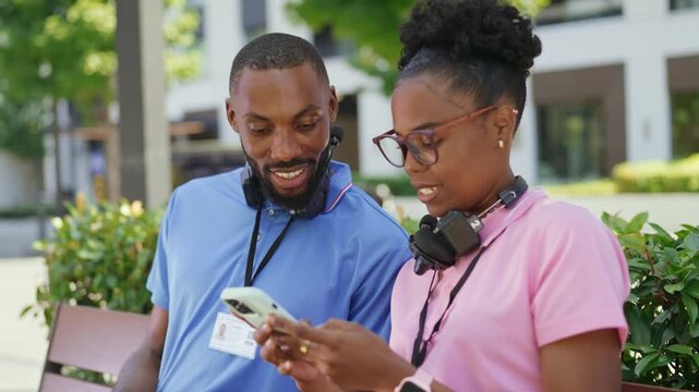 Two couriers comparing delivery orders on a smartphone while taking a break outdoors. Parcel delivery, teamwork, and daily logistics coordination.