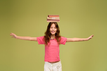 Joyful girl balancing books on her head while wearing stylish comfy attire