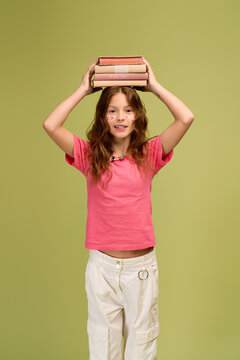 Charming little girl joyfully balancing books while dressed in trendy casual outfit