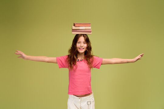 Joyful girl balancing books on her head while wearing stylish comfy attire