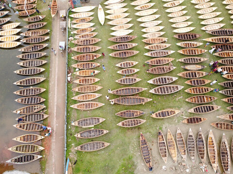 Aerial view of the Boat Market with numerous wooden boats arranged in rows on the grassy riverbank and along the water in Manikganj, Bangladesh.