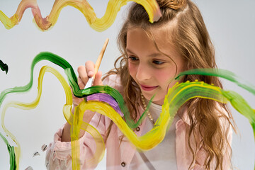 Little girl joyfully painting colorful swirls with a brush on a bright canvas © LIGHTFIELD STUDIOS