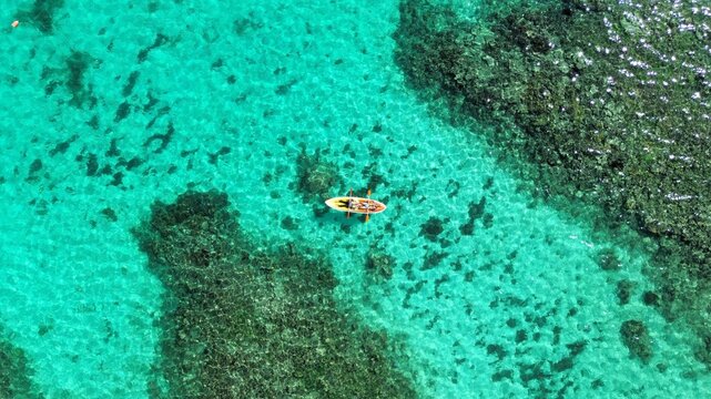 Karimunjawa, Central Java, Indonesia - 17 July 2025: Aerial view of a person paddling a kayak over vibrant coral reefs and clear turquoise waters of Karimunjawa National Park.