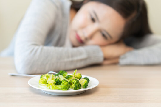 Diet in bored concept, Ketogenic, Low carb, Intermittent Fasting asian young woman dieting, looking at broccoli salad plate tired with eat fresh vegetables. Nutrition clean, healthy food good taste.