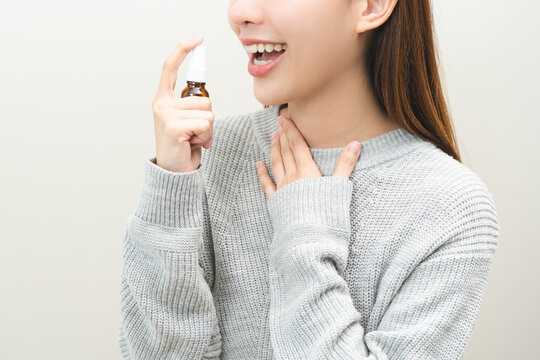 Health care treatment sore throat concept, sick pain asian young woman have cough symptom holding medicine bottle, using spray in mouth to protect disease from bacteria, illness from virus infection.