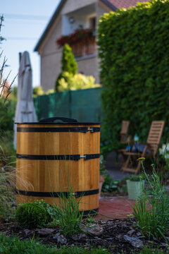 Wooden ice bath barrel for cold plunge therapy standing in a green garden. Traditional outdoor cooling tub next to a house for biohacking, wellness and post sauna recovery.