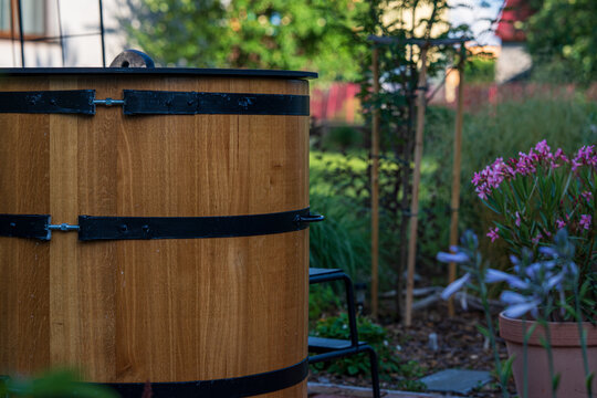 Wooden ice bath barrel for cold plunge therapy standing in a green garden. Traditional outdoor cooling tub next to a house for biohacking, wellness and post sauna recovery.