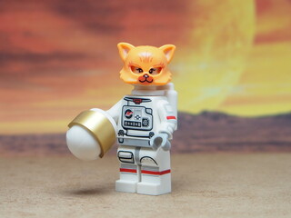 Naklejka premium Indonesia - May 16, 2025 : Mini toy of action figure at table with blurred background. Miniature photography concept design. Minifigure of Orange Cat character wearing astronaut suit at outer space.