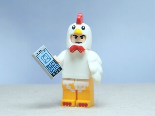 Naklejka premium Indonesia - May 16, 2025 : Mini toy of action figure at table with blurred background. Miniature photography concept design. Minifigure of chicken character hold smartphone on hand. Smart farm concept