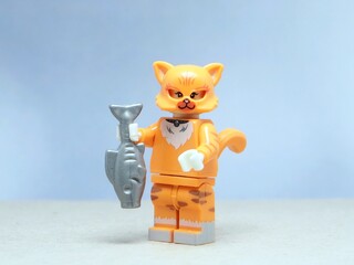 Fototapeta premium Indonesia - May 16, 2025 : Mini toy of action figure at table with blurred background. Miniature photography concept design. Minifigure of orange cat character hold the fresh fish.