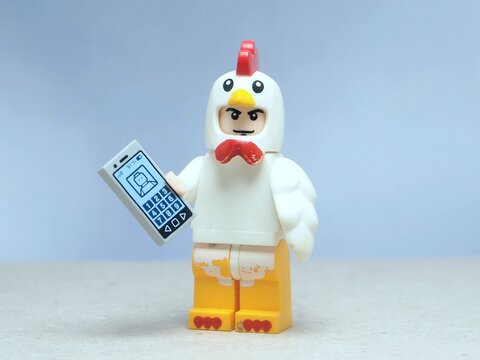 Indonesia - May 16, 2025 : Mini toy of action figure at table with blurred background. Miniature photography concept design. Minifigure of chicken character hold smartphone on hand. Smart farm concept