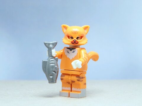 Indonesia - May 16, 2025 : Mini toy of action figure at table with blurred background. Miniature photography concept design. Minifigure of orange cat character hold the fresh fish.