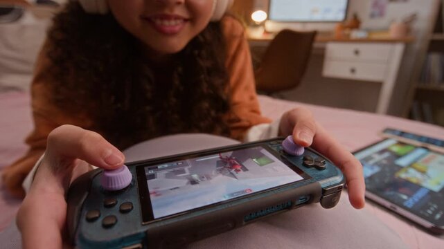 Asian teenager playing video game on handheld console while lying on bed. Footage is perfect for marketing gaming accessories, mobile apps, and modern youth entertainment