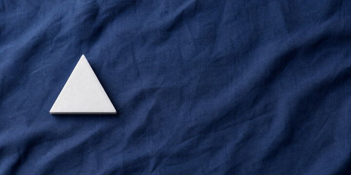 Single white equilateral triangle object on deep blue linen, calm still life for editorial concept