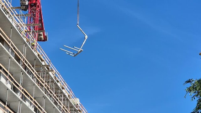 Wide shot of a crane hoisting a Doka Staxo load-bearing tower fork while workers in full PPE install collective edge protection safety railings on an upper floor.