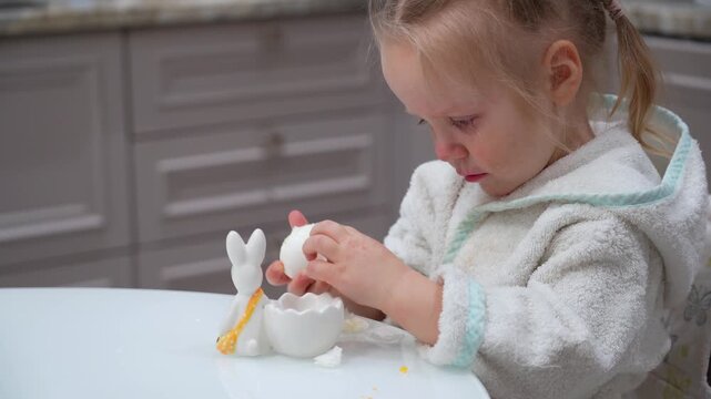 Distressed Toddler Attempting to Peel Boiled Egg at Kitchen Table with Ceramic Rabbit Decoration