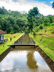Fototapeta premium Peaceful Irrigation Canal with Small Bridge in Mountain Countryside 