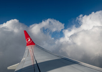Obraz premium Caselle airport, turin province, italy. August 1, 2025. Turkish airlines aircraft wing flying over caselle airport, turin, italy. Experiencing travel, aviation, and clear blue sky with white clouds