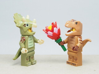 Fototapeta premium Indonesia - March 4, 2026 : Mini toy of action figure at outdoor with blur background. Miniature photography concept design. Minifigure of T-rex Dino character give bouquet of flower to triceratops.