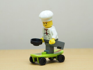 Fototapeta premium Indonesia - February 10, 2026 : Mini toy of action figure at outdoor with blur background. Miniature photography concept design. Minifigure of chef character playing skate board at sport arena.