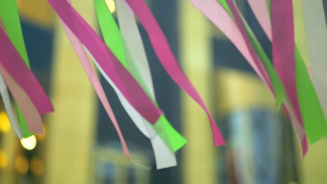 Vibrant pink green white ribbons sway gently in breeze. Soft motion highlights festive decorations. Blurred background suggests street event. Ideal for birthday celebrations