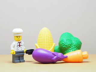 Naklejka premium Indonesia - February 10, 2026 : Mini toy of action figure at outdoor with blur background. Miniature photography concept design. Minifigure of chef character with eggplant, corn, broccoli and carrot.