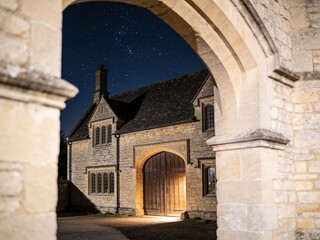 Fototapeta premium Cinematic shot of a rustic ancient stone inn exterior and wooden door against night sky copy space