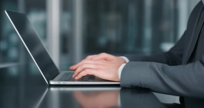 Businessman typing on laptop in modern office setting at glass table