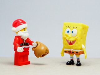 Obraz premium Indonesia - November 23, 2025 : Mini toy of action figure at table with blurred background. Miniature photography concept design. Minifigure of Spongebob and Santa Claus character. Christmas theme.