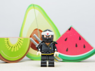 Fototapeta premium Indonesia - December 5, 2025 : Mini toy of action figure at outdoor with blurred background. Miniature photography concept design. Minifigure of Ninja Go character with Avocado, Water Melon and Kiwi.