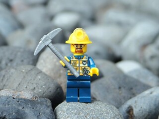 Fototapeta premium Indonesia - November 30, 2025 : Mini toy of action figure at outdoor with blurred background. Miniature photography concept design. Minifigure of miner worker at rock mountain with pickaxe and helmet.