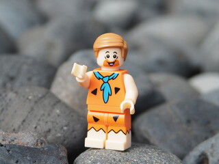 Obraz premium Indonesia - November 30, 2025 : Mini toy of action figure at outdoor with blurred background. Miniature photography concept design. Minifigure of Fred Flintstone character from film at rock mountain.