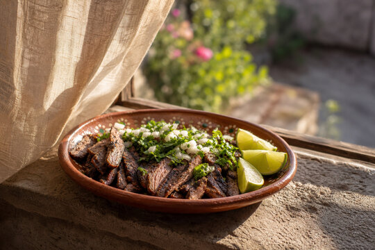 Clay dish of grilled carne asada with cilantro, onion, and lime on stone ledge, authentic Mexican taco filling and food presentation concept