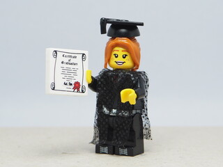 Fototapeta premium Indonesia - November 24, 2025 : Mini toy of action figure at table with blurred background. Miniature photography concept design. Minifigure ofwoman student with graduation gown, cap and certificate.