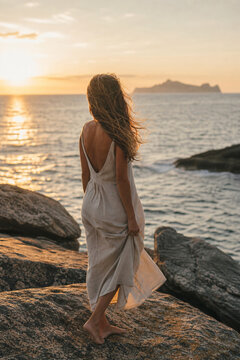 Young woman standing on beach rocks gazing at ocean, travel and freedom portrait concept.