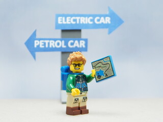 Fototapeta premium Indonesia - April 14, 2025 : Mini toy of action figure at table with blurred background. Auto photography concept design. Minifigure of people character with roadsign. Electrical EV Car vs Petrol Car.