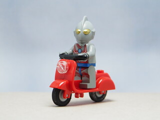 Obraz premium Indonesia - April 14, 2025 : Mini toy of action figure at outdoor with blur background. Miniature photography concept design. Minifigure of Ultra Man character from fiction film. Riding the scooter.
