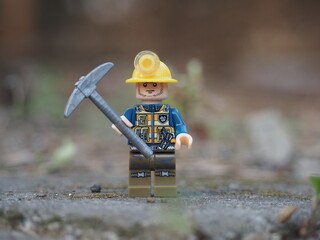 Fototapeta premium Indonesia - November 30, 2025 : Mini toy of action figure at outdoor with blurred background. Miniature photography concept design. Minifigure of miner worker at rock mountain with pickaxe and helmet.