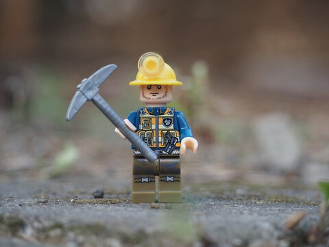Indonesia - November 30, 2025 : Mini toy of action figure at outdoor with blurred background. Miniature photography concept design. Minifigure of miner worker at rock mountain with pickaxe and helmet.