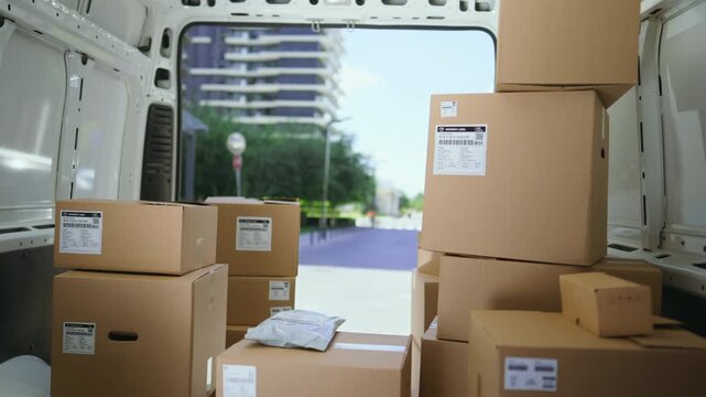 Boxes are stacked inside a delivery truck parked near a building. Couriers are busy unloading packages and arranging them for delivery.