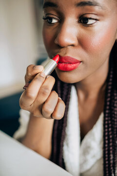 Close up portrait of african american woman putting on red lipstick 