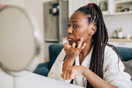 Portrait of african american woman applying foundation at home