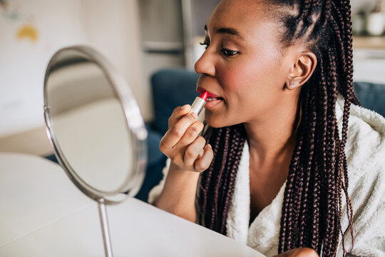Home closeup portrait of african american woman putting on lipstick 