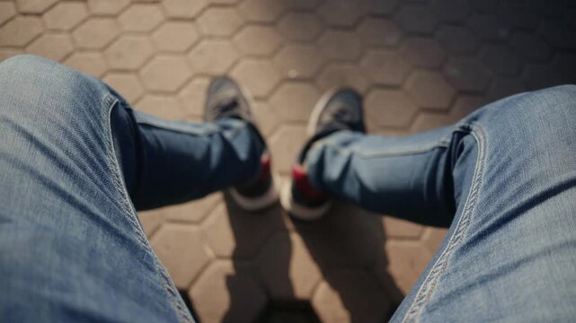 Man's legs in jeans and sneakers moving slightly on patterned pavement outdoors.