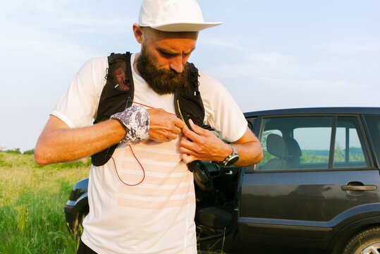 A trail runner puts on a running vest next to his car