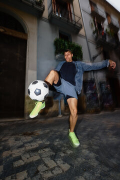 Man practices soccer skills on city street at night