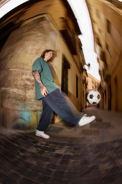 Man kicks soccer ball in narrow street during daytime
