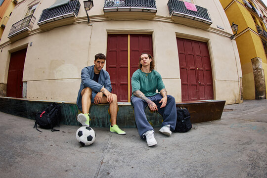 Friends sit on steps with soccer ball in city street