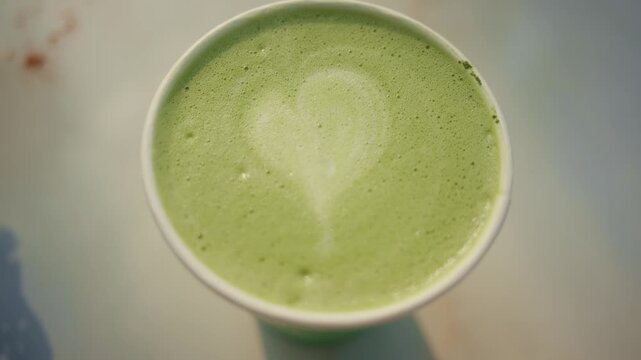Green tea matcha latte art in paper cup on white table with heart shape foam from top view dynamic.