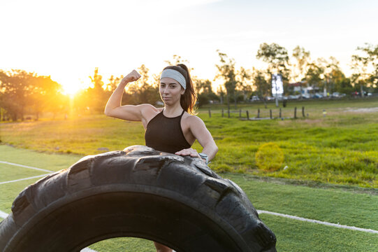 Strong athlete flexing her biceps beside a training tire